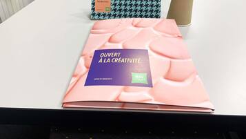 Una mesa con un libro titulado 'OUVERT À LA CRÉATIVITÉ' y una caja estampada con diseño de piedritas y la palabra 'BIENVENUE'.