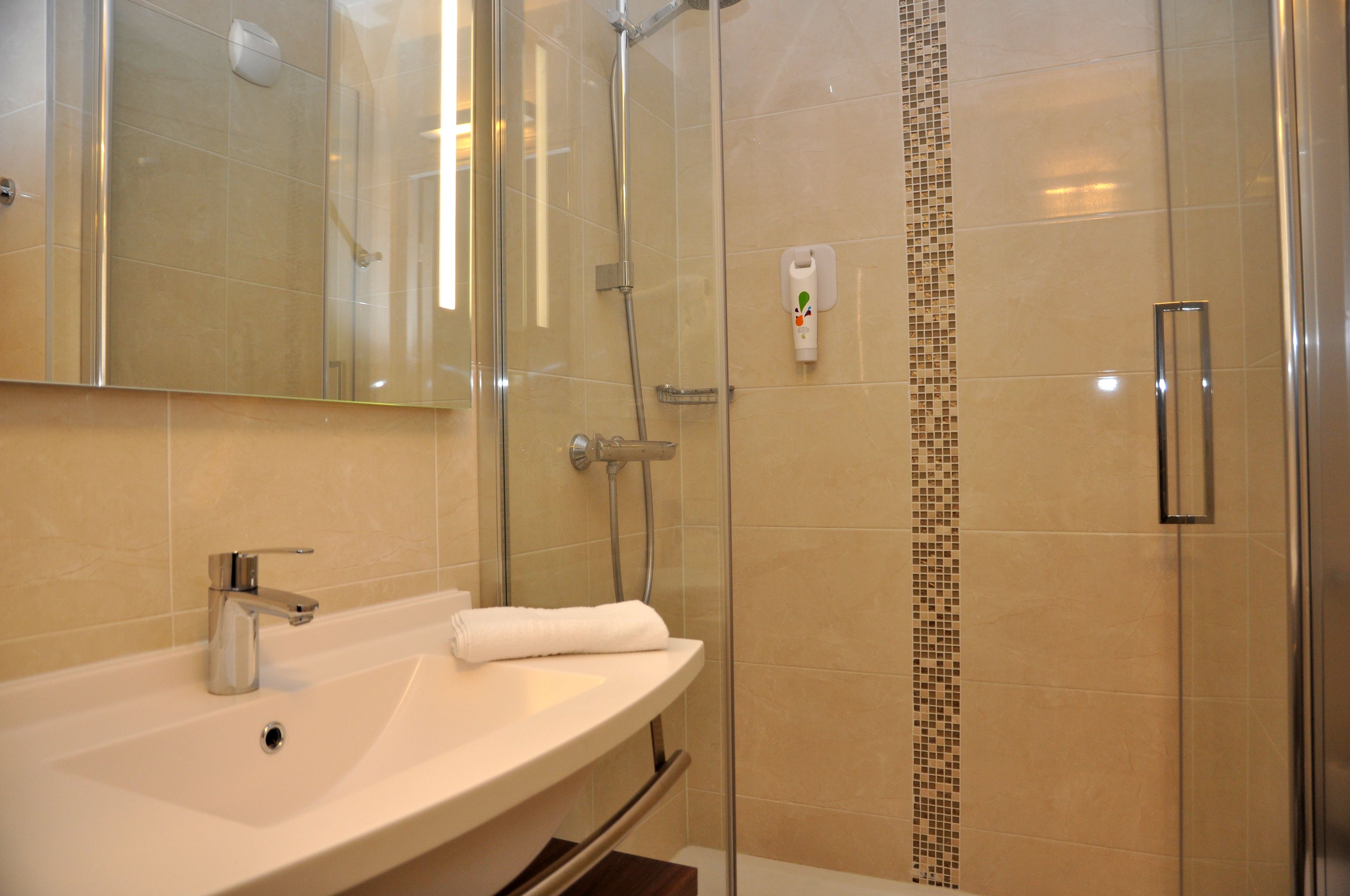 Een moderne badkamer met een douche met glazen wand, een witte wastafel en een spiegel erboven.