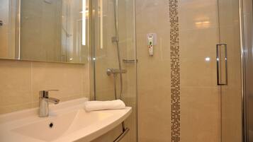 Een moderne badkamer met een douche met glazen wand, een witte wastafel en een spiegel erboven.