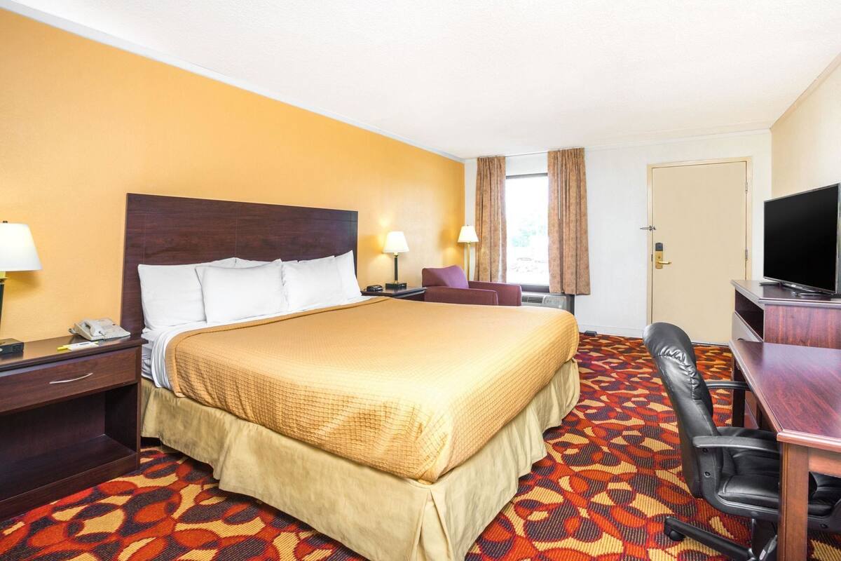 Une chambre d’hôtel avec un grand lit, un bureau avec une chaise, une télévision et une porte.