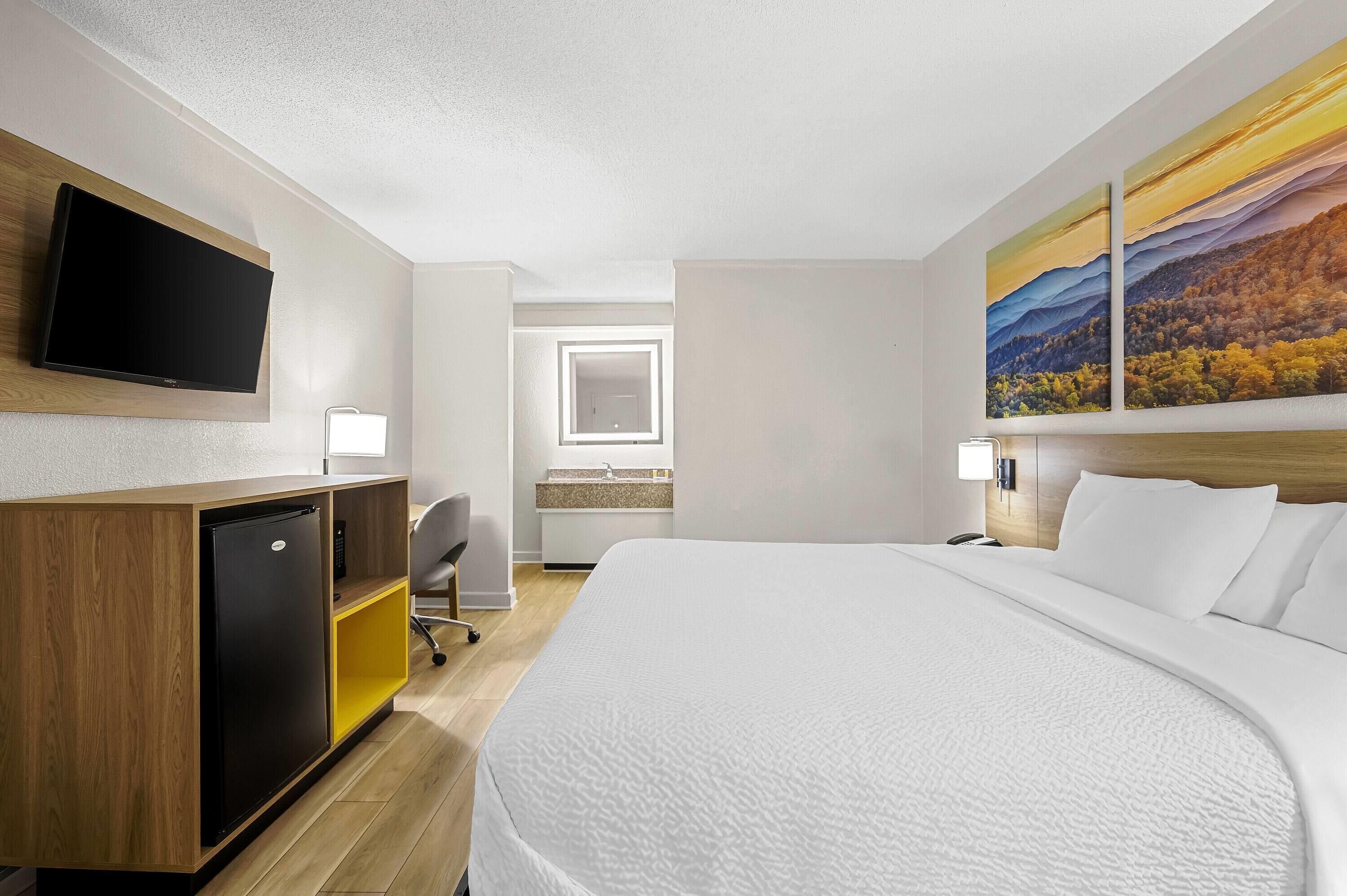 A hotel room with a bed, a desk with a computer, a TV, and a painting on the wall.