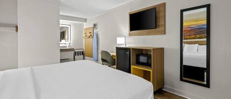 Habitación de hotel con una cama grande, un escritorio con computadora, un televisor en la pared y vista de un paisaje por la ventana.