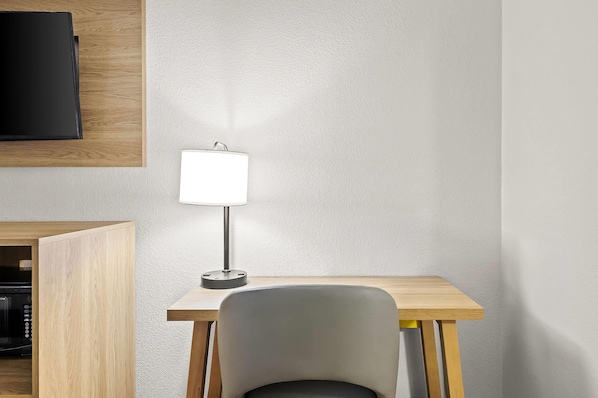 A modern room with a wooden desk, a grey chair, a white lamp, and a flat-screen TV mounted on the wall.