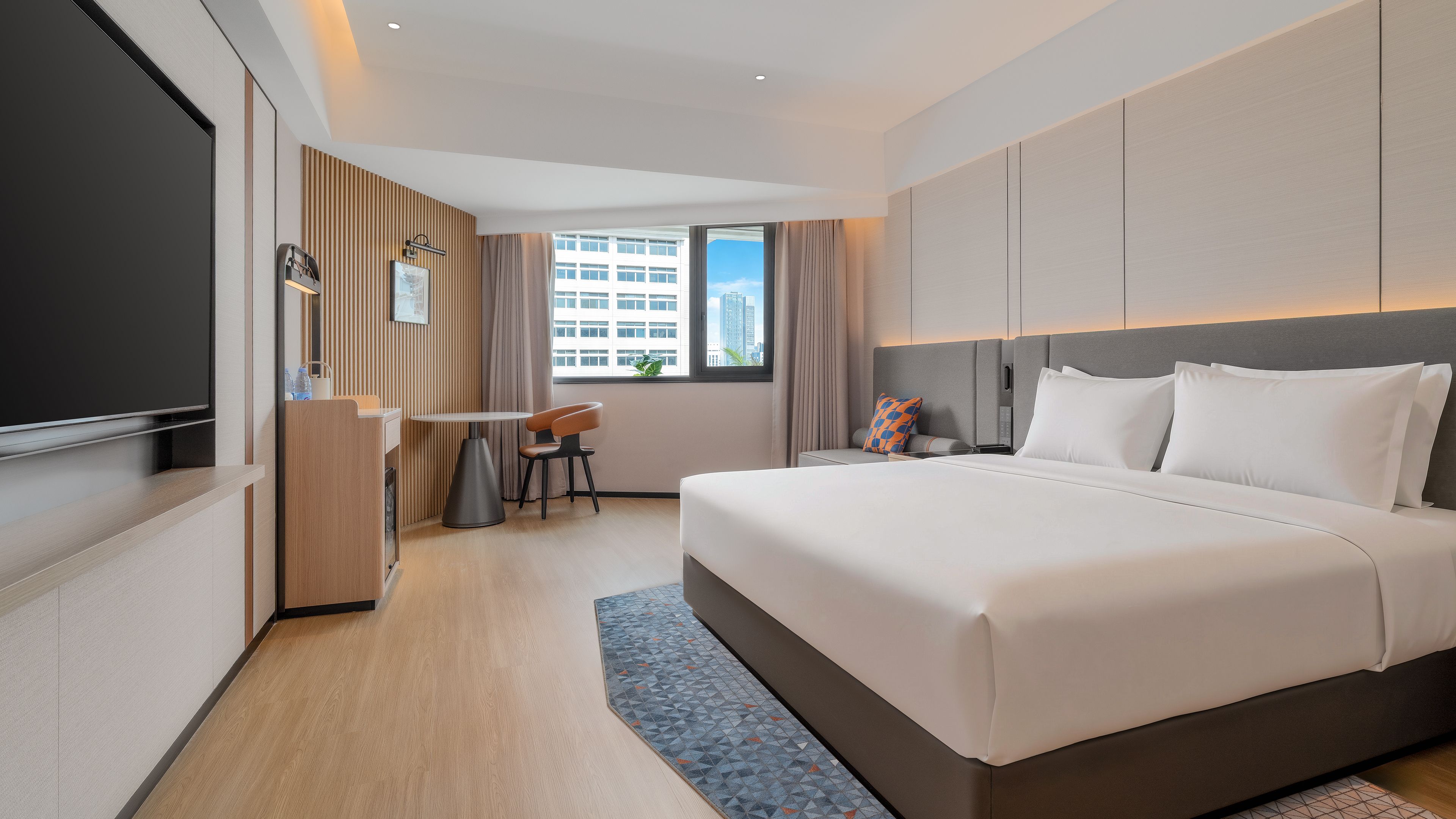 A modern hotel room with a large bed, a desk, and a view of the city.