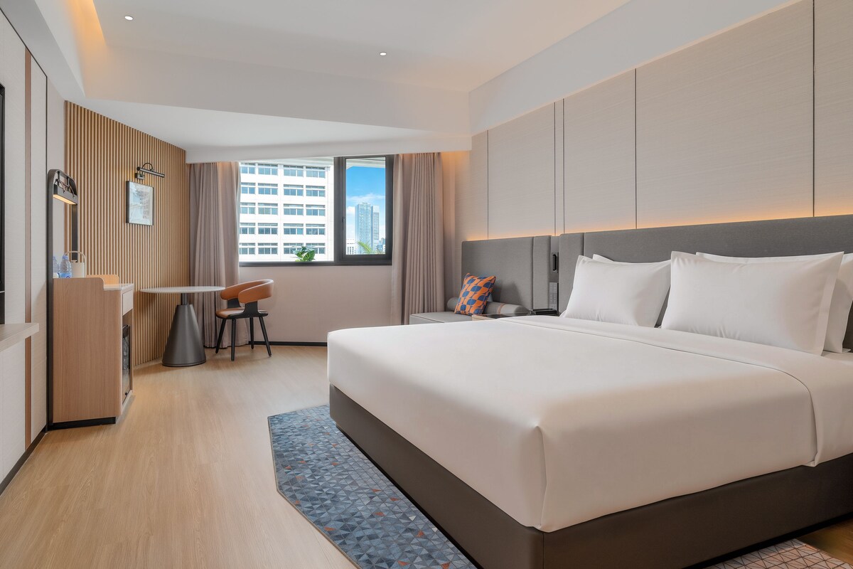 A modern hotel room with a large bed, a desk, and a view of the city.