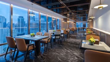 A modern dining area with tables and chairs, large windows, and a city view.