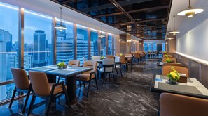 A modern dining area with tables and chairs, large windows, and a city view. - Holiday Inn Express Shenzhen Luohu Port by IHG (Shenzhen)