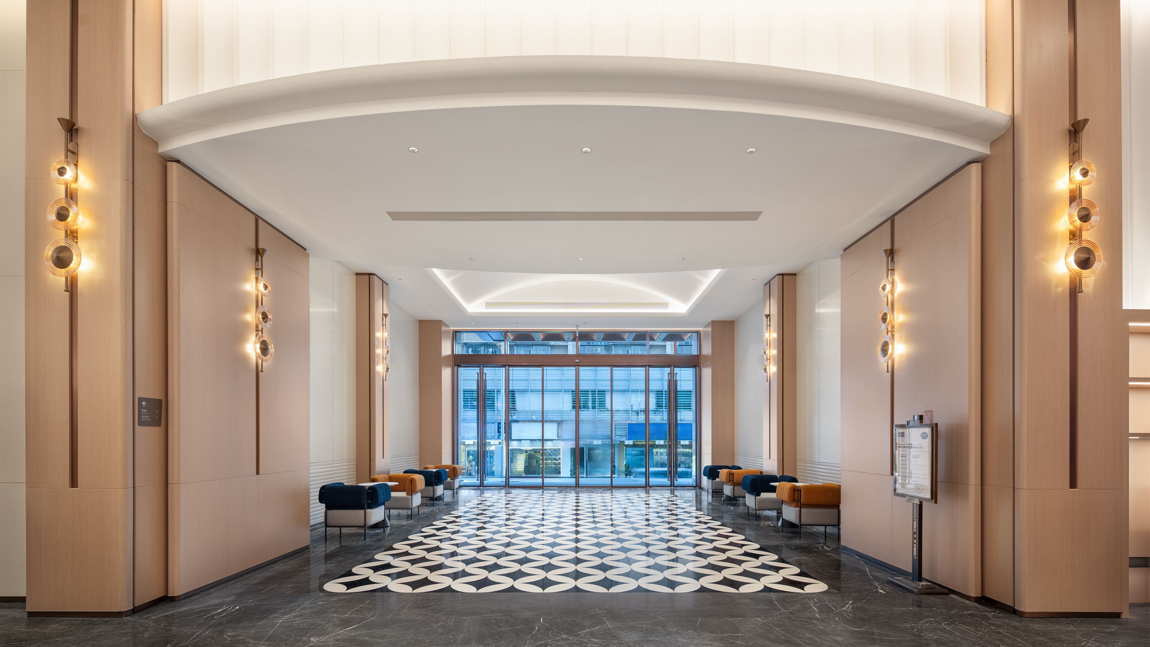 A hotel lobby with a patterned floor, seating area, and a view through the glass doors.