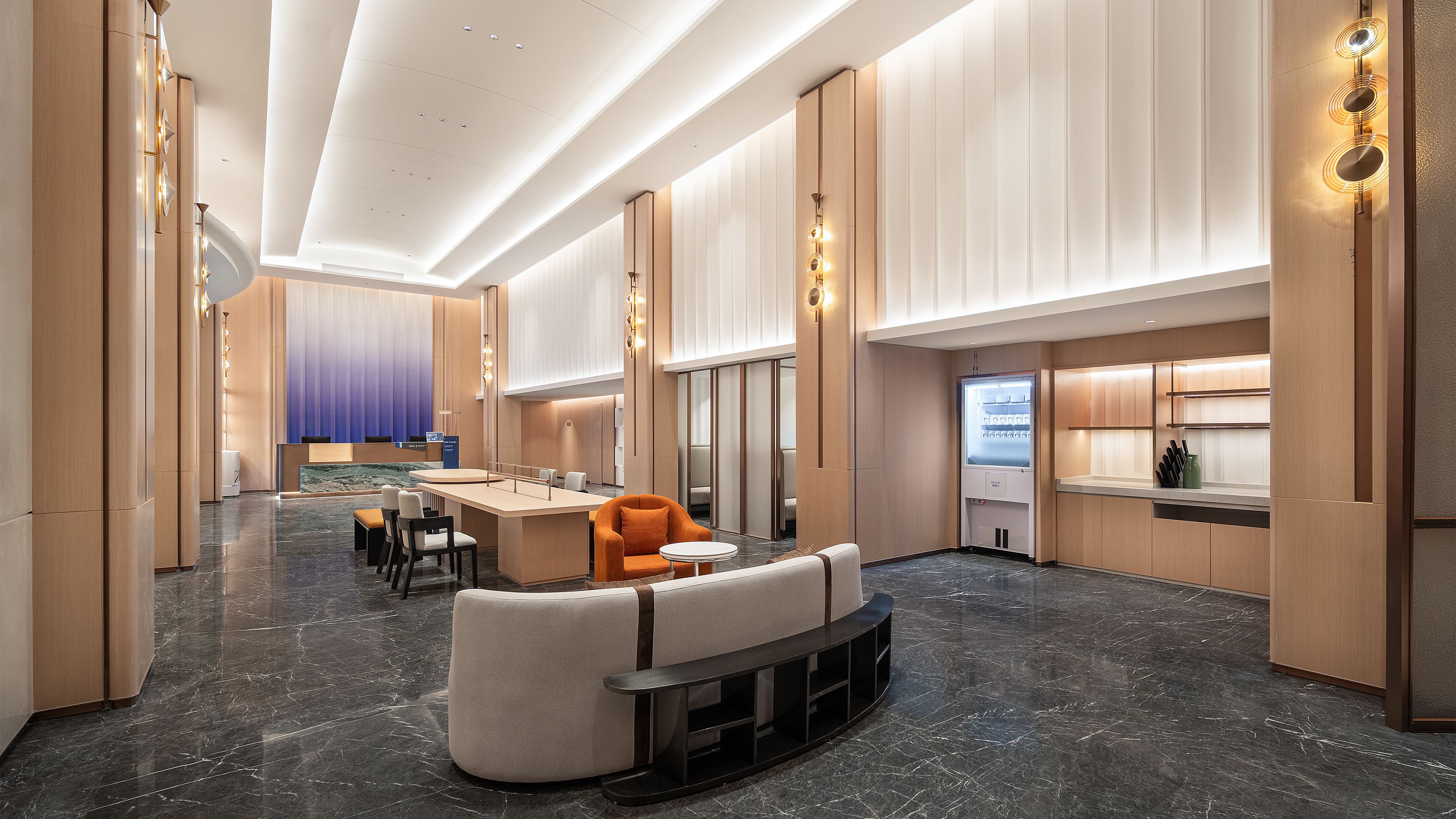 A modern hotel lobby with a marble floor, seating area, and a kitchenette.