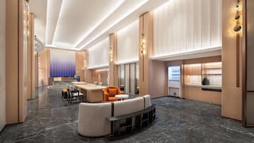 A modern hotel lobby with a marble floor, seating area, and a kitchenette.