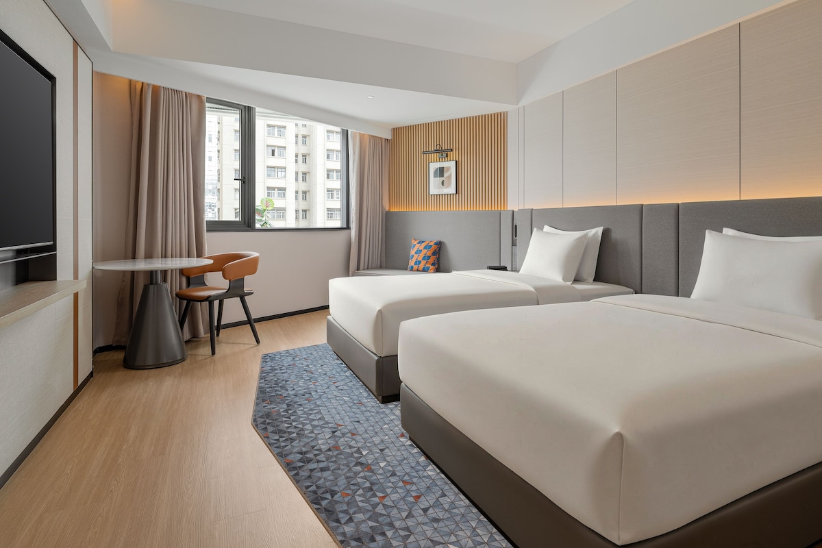 A hotel room with two beds, a desk, and a TV.