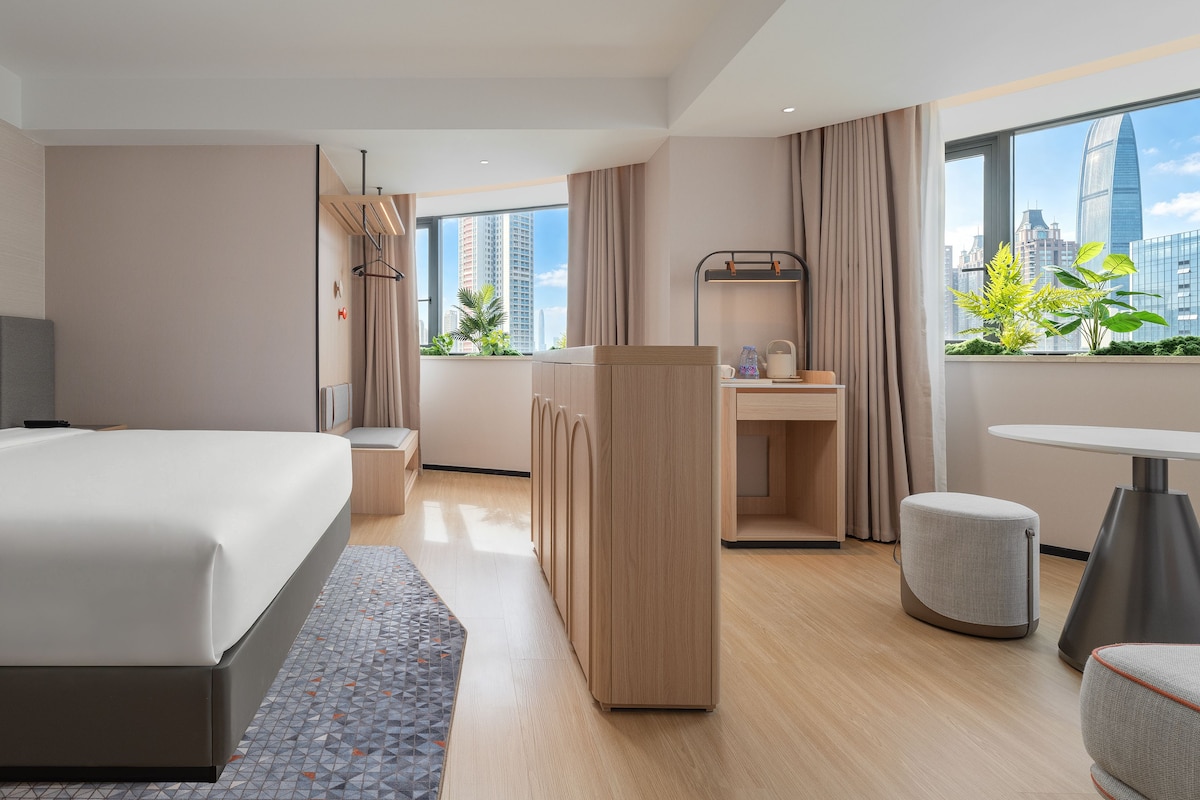 A modern hotel room with a large bed, a desk, and a view of the city skyline.