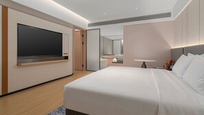 A modern hotel room with a large bed, a flat-screen TV mounted on the wall, a bedside table with a lamp, and a bathroom visible through an open door. - Holiday Inn Express Shenzhen Luohu Port by IHG (Shenzhen)