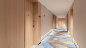 Pasillo de hotel con puertas de madera, alfombra estampada y un cartel que indica la habitación 702.