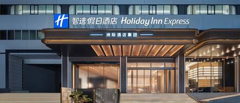 Una entrada de hotel moderna con un vestíbulo techado, puertas de vidrio grandes y un letrero que indica que es un Holiday Inn Express.