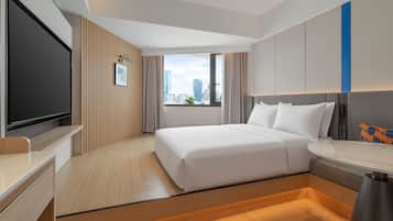Een hotelkamer met een bed, een bureau, een televisie en een raam met uitzicht op de stad.