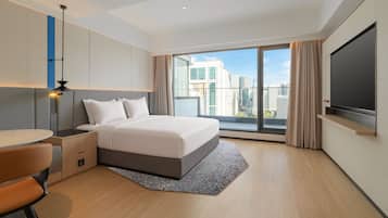 Ein modernes Hotelzimmer mit einem großen Bett, einem Schreibtisch, einem Flachbildfernseher und Blick auf die Stadt.