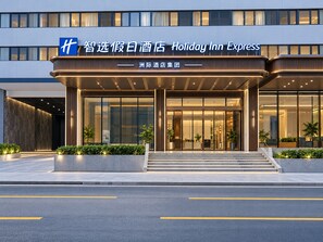 Entrada de un hotel Holiday Inn Express con diseño moderno, destacando un cartel llamativo y una fachada bien iluminada.