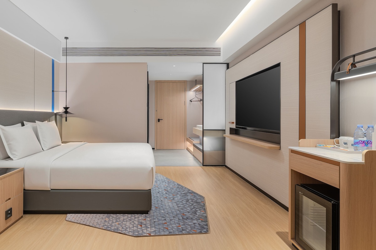 A modern hotel room with a bed, bedside table, TV, and a minibar.