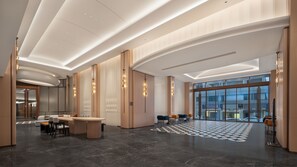 A modern hotel lobby with a reception desk, seating area, and large windows offering a view of the city.