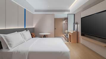 A modern hotel room with a bed, a small round table, a TV, and a bathroom with a mirror and sink.