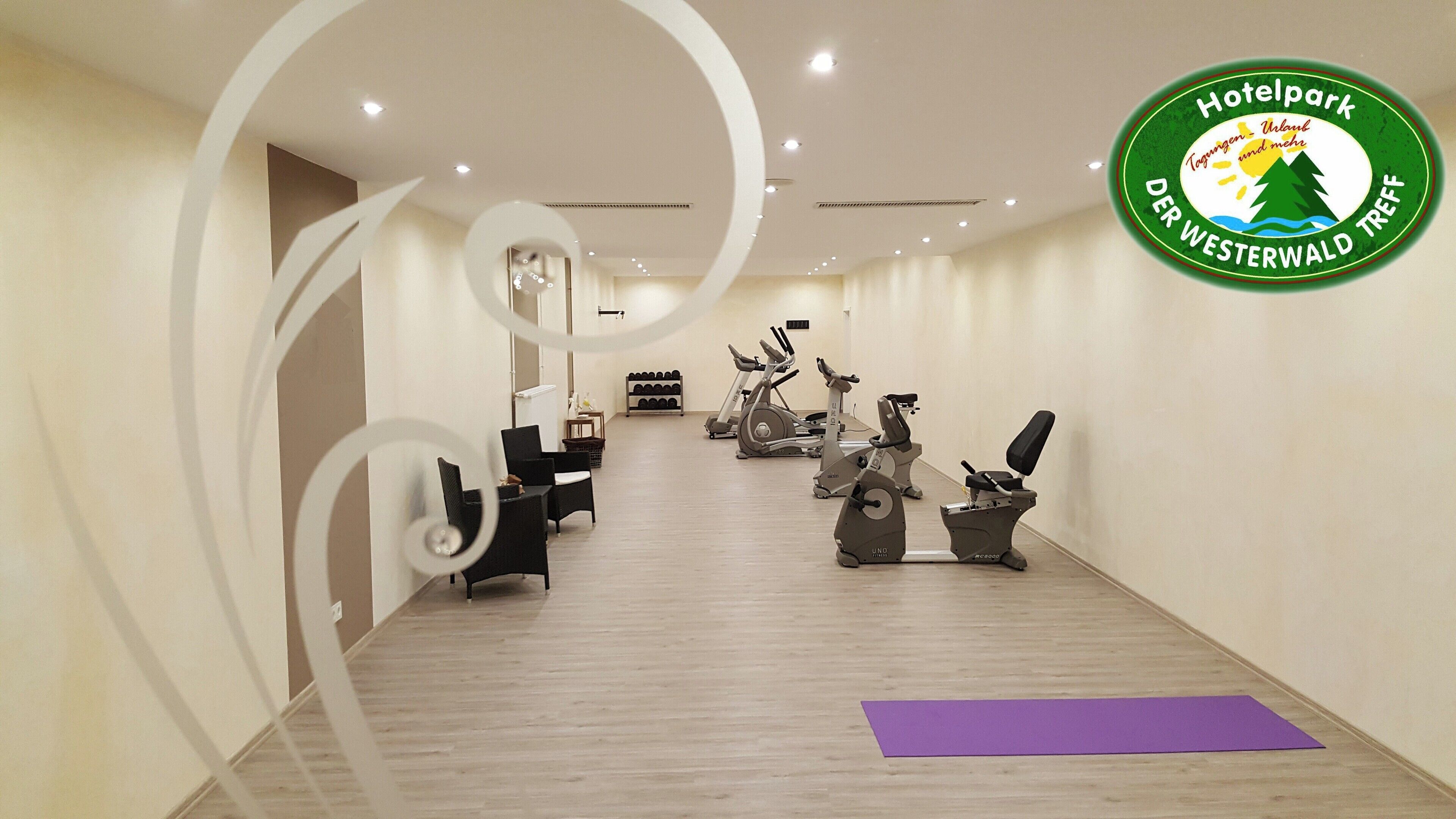 Une salle de sport d’hôtel équipée de matériel d’exercice, avec un tapis violet et un logo sur le mur.