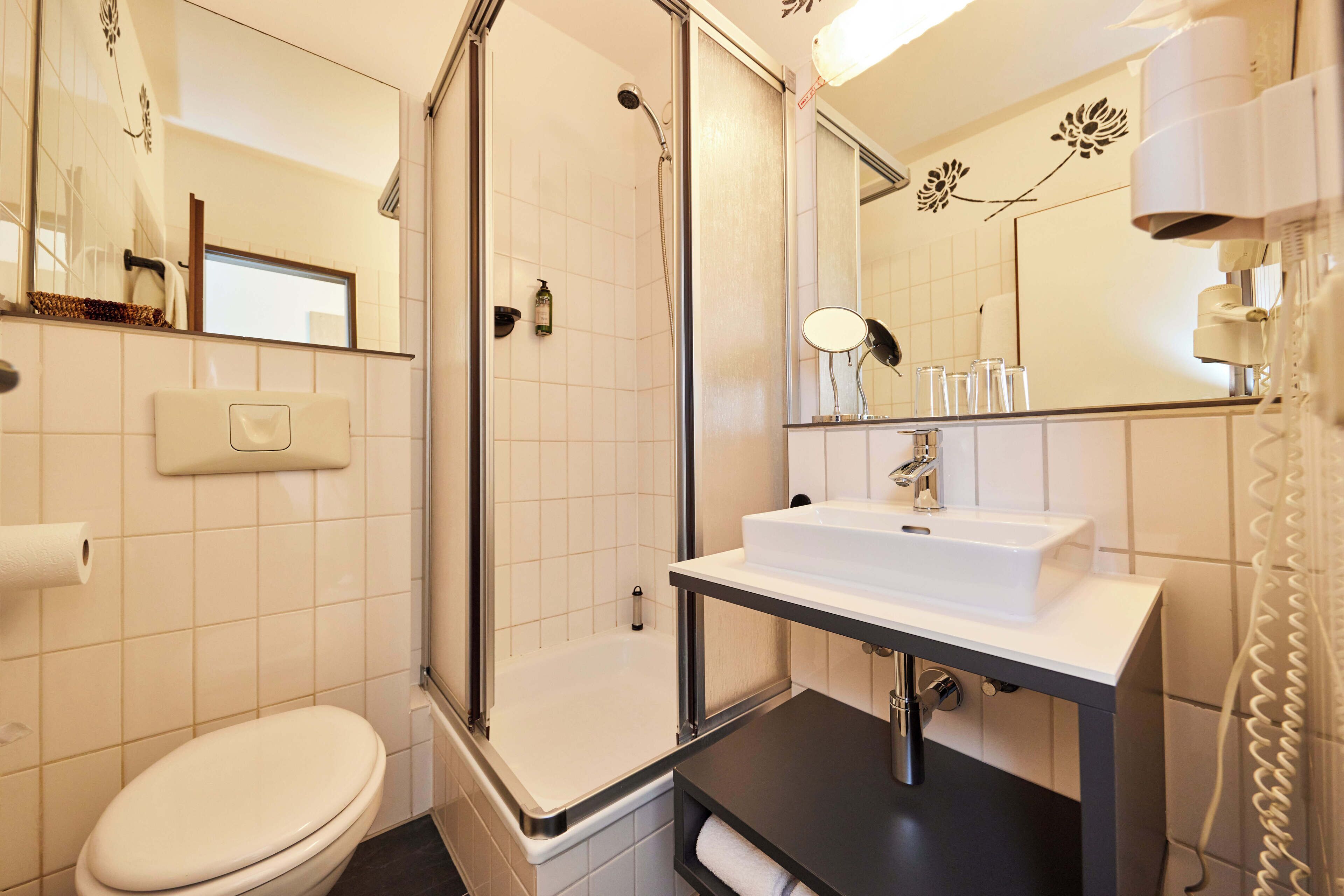 A modern bathroom with a toilet, a shower with a glass door, a sink with a mirror, and a towel rack.
