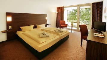 A hotel room with a large bed, a desk with a TV, and a balcony with a chair.
