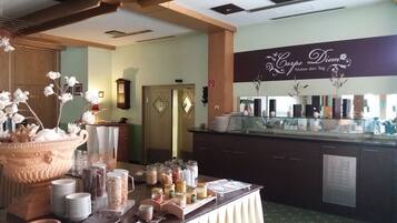A buffet setup with a variety of food items and condiments, a clock on the wall, and a decorative vase with flowers.