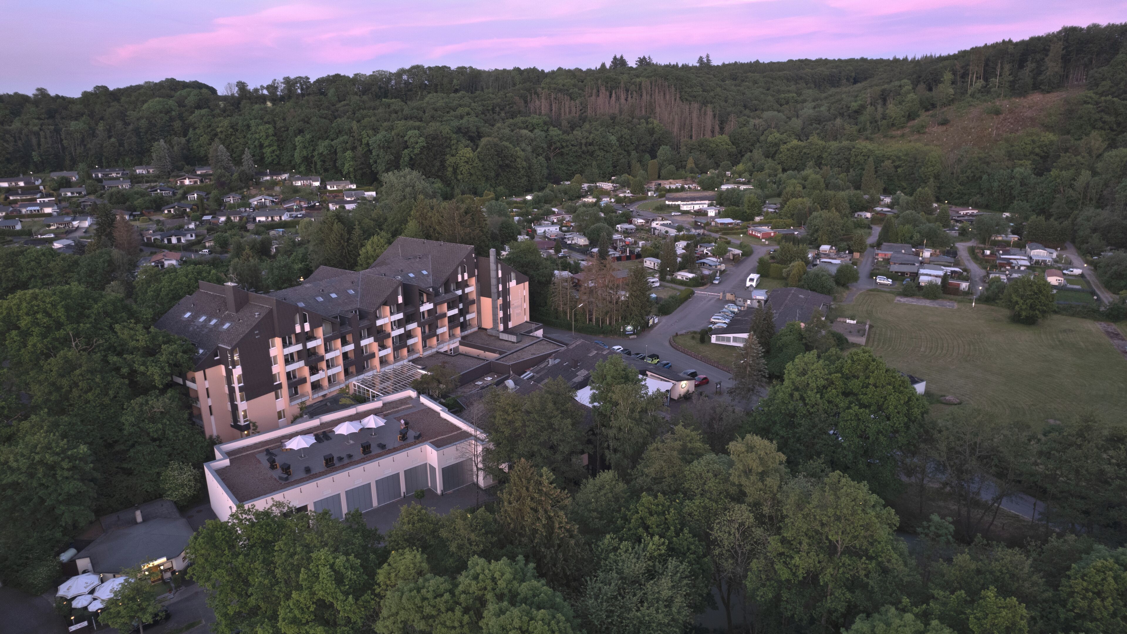 An aerial view of a residential area with a large building featuring multiple floors, a parking lot, and surrounding greenery.