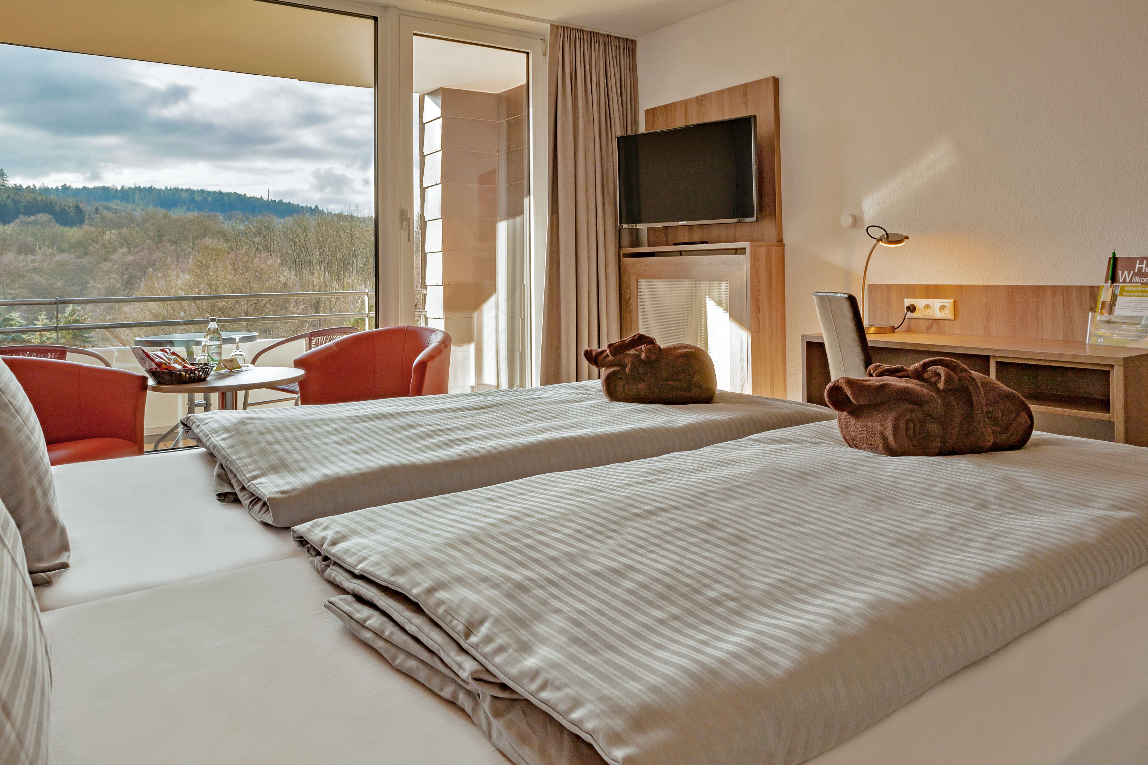 Habitación de hotel con dos camas, televisión, escritorio y vistas al exterior.