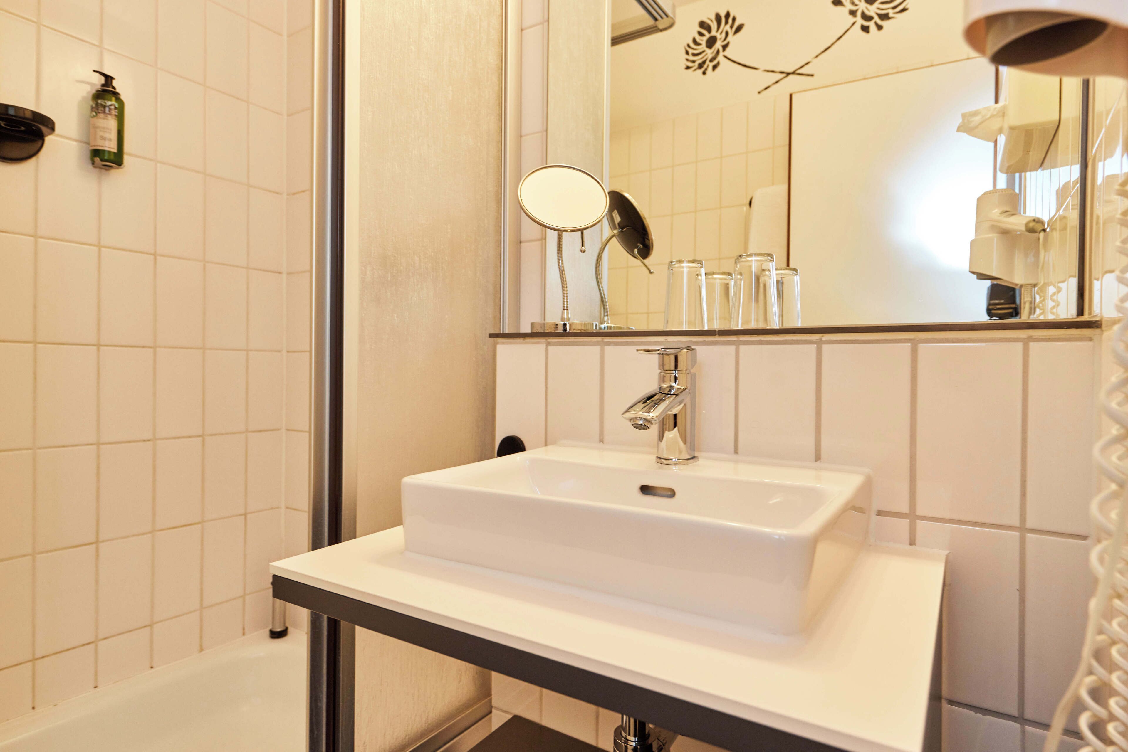 A bathroom with a white sink, mirror, and a shower area.