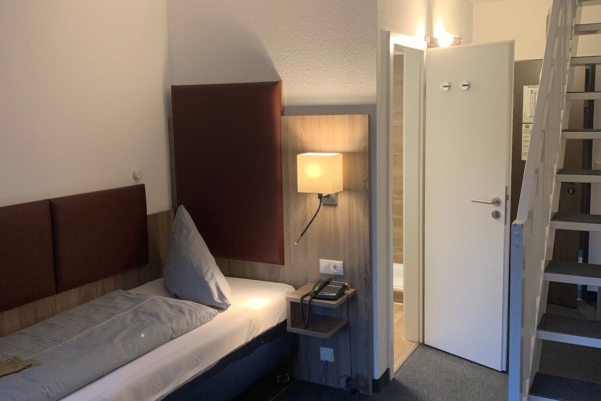 A hotel room with a bed, bedside table with a lamp, a phone, and a door leading to a staircase.