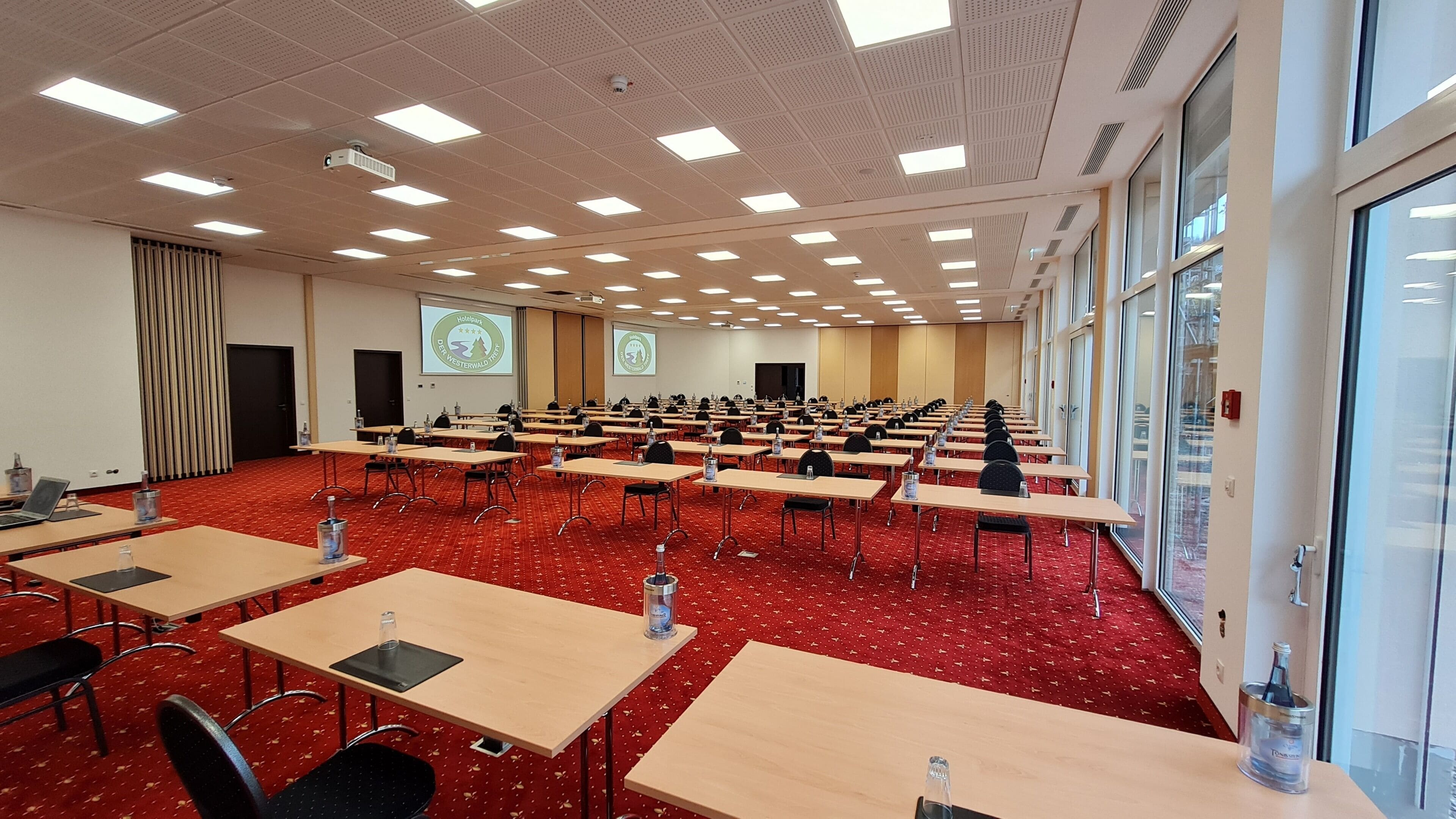 A conference room with rows of tables, chairs, and a projector screen.