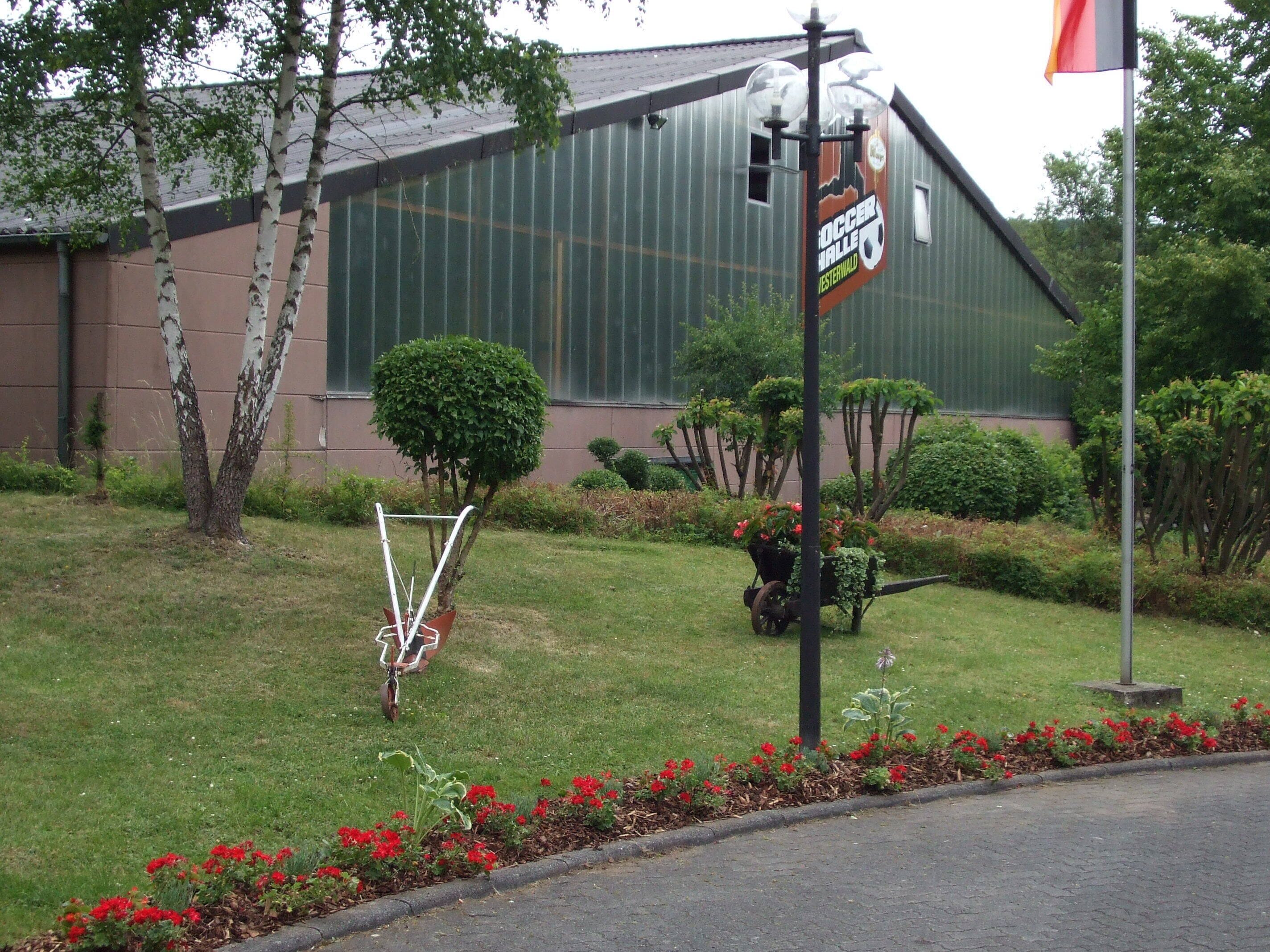 A building with a sign for a soccer field and a garden with red flowers and a small tree.
