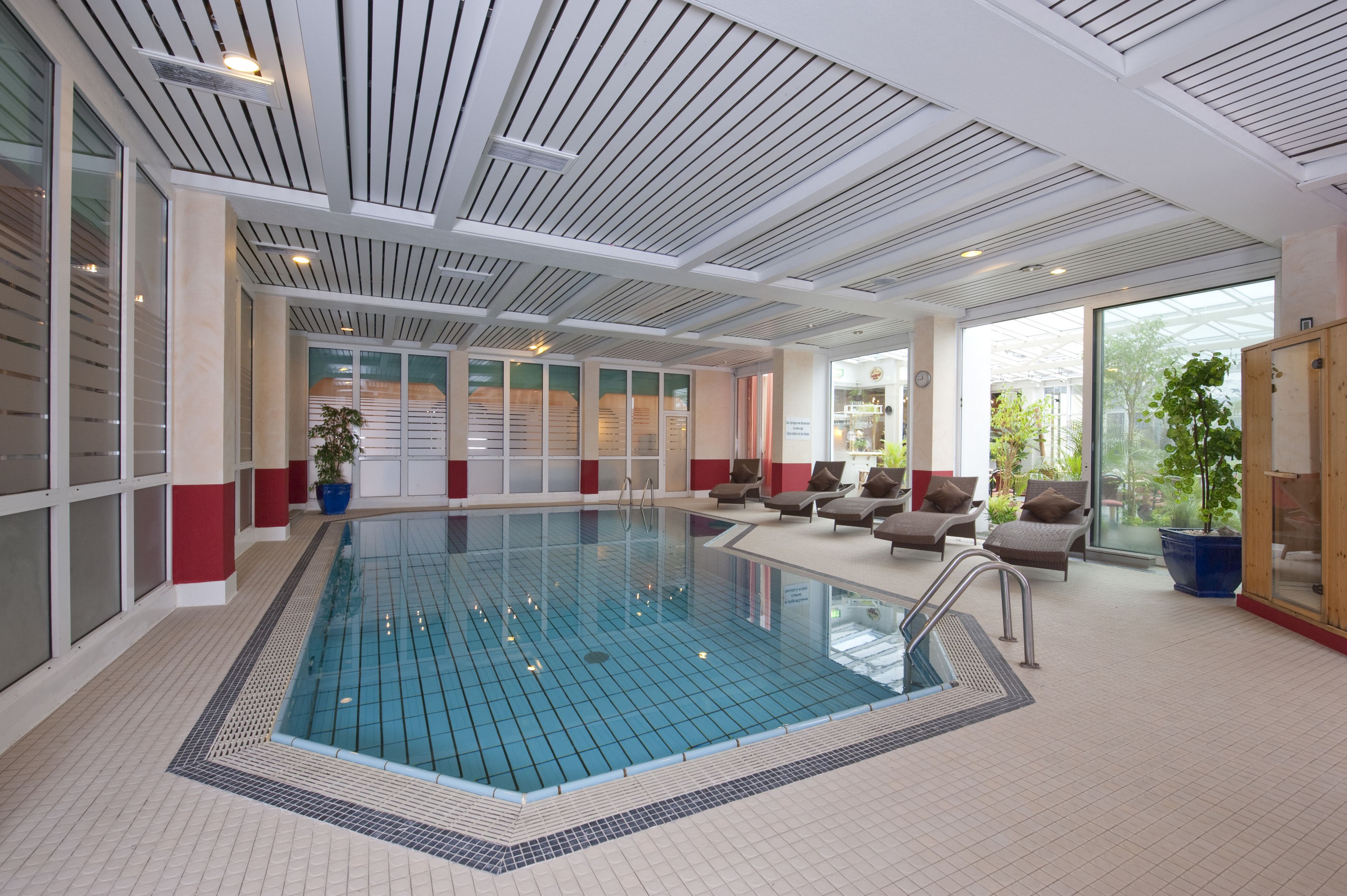 Une piscine intérieure moderne, avec de l’eau cristalline, entourée de chaises longues et de plantes en pot.