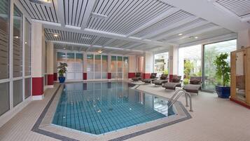 Une piscine intérieure moderne, avec de l’eau cristalline, entourée de chaises longues et de plantes en pot.