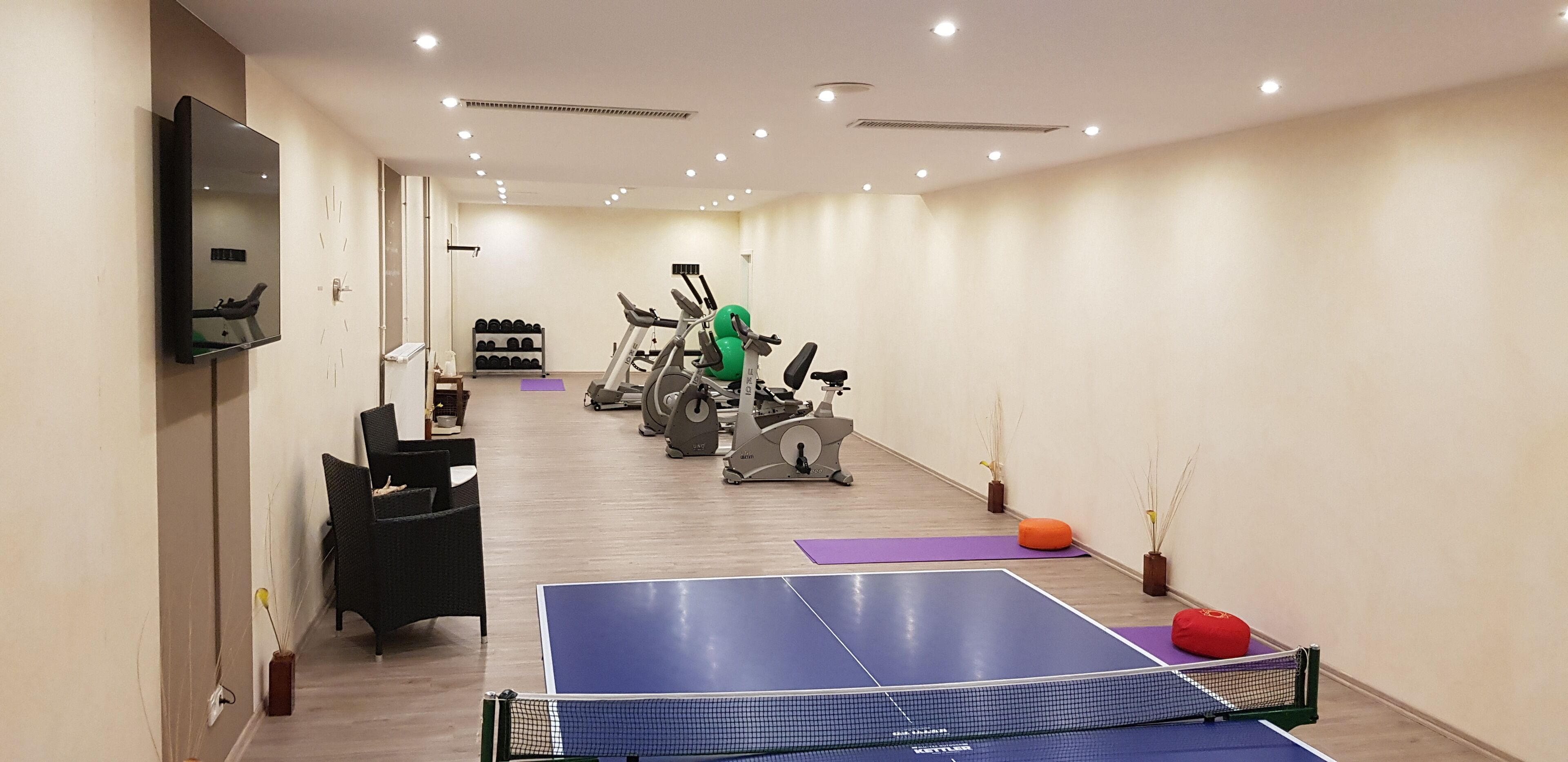 A gym with exercise equipment, a ping pong table, and a TV on the wall.