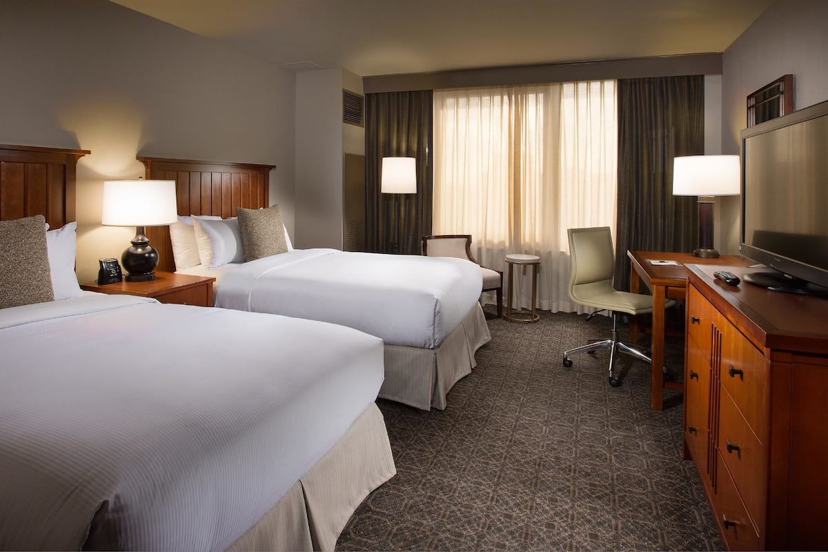 A hotel room with two beds, a desk with a television, a chair, and a small table.