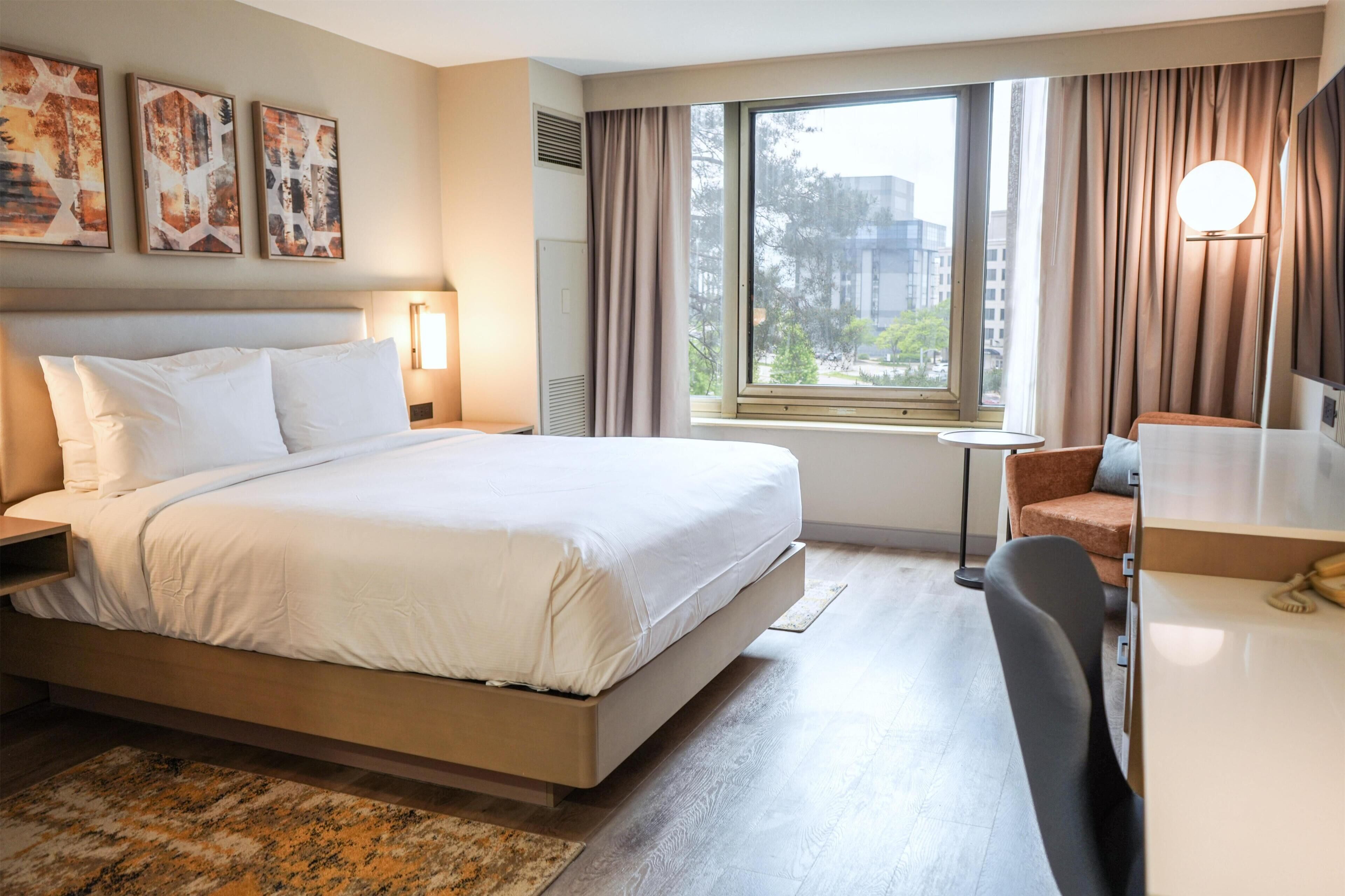 Een hotelkamer met een bed, een bureau, een stoel, een raam met gordijnen en kunst aan de muur.
