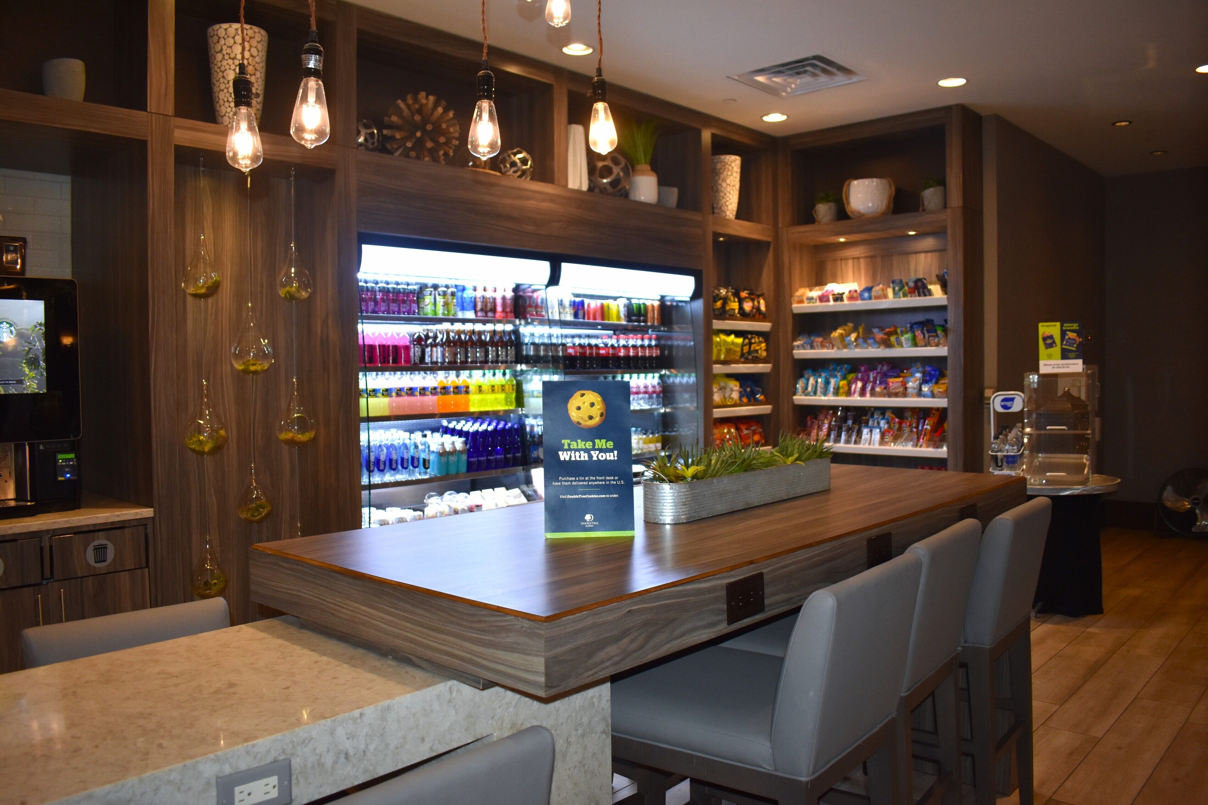 Un espace bar doté d’un comptoir en bois, de tabourets de bar et d’un réfrigérateur-vitrine rempli de boissons.