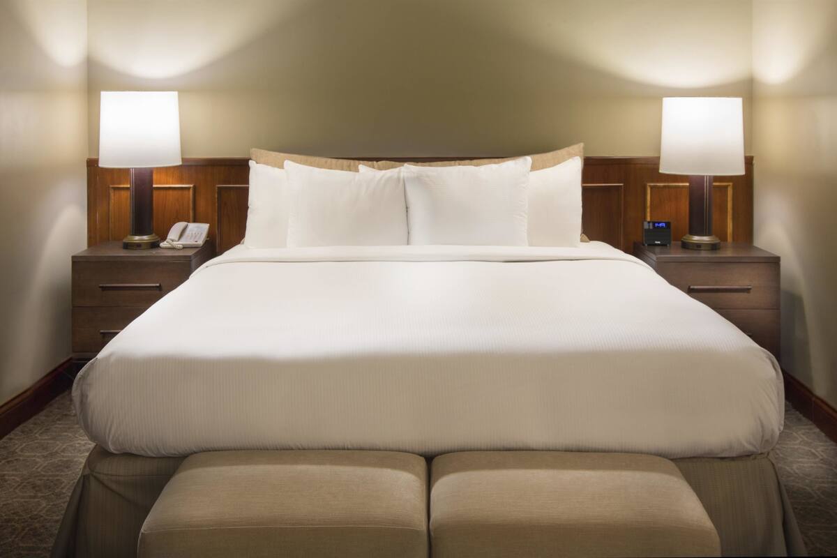 A hotel room with a large bed, two bedside tables, a nightstand, a lamp, and a phone.