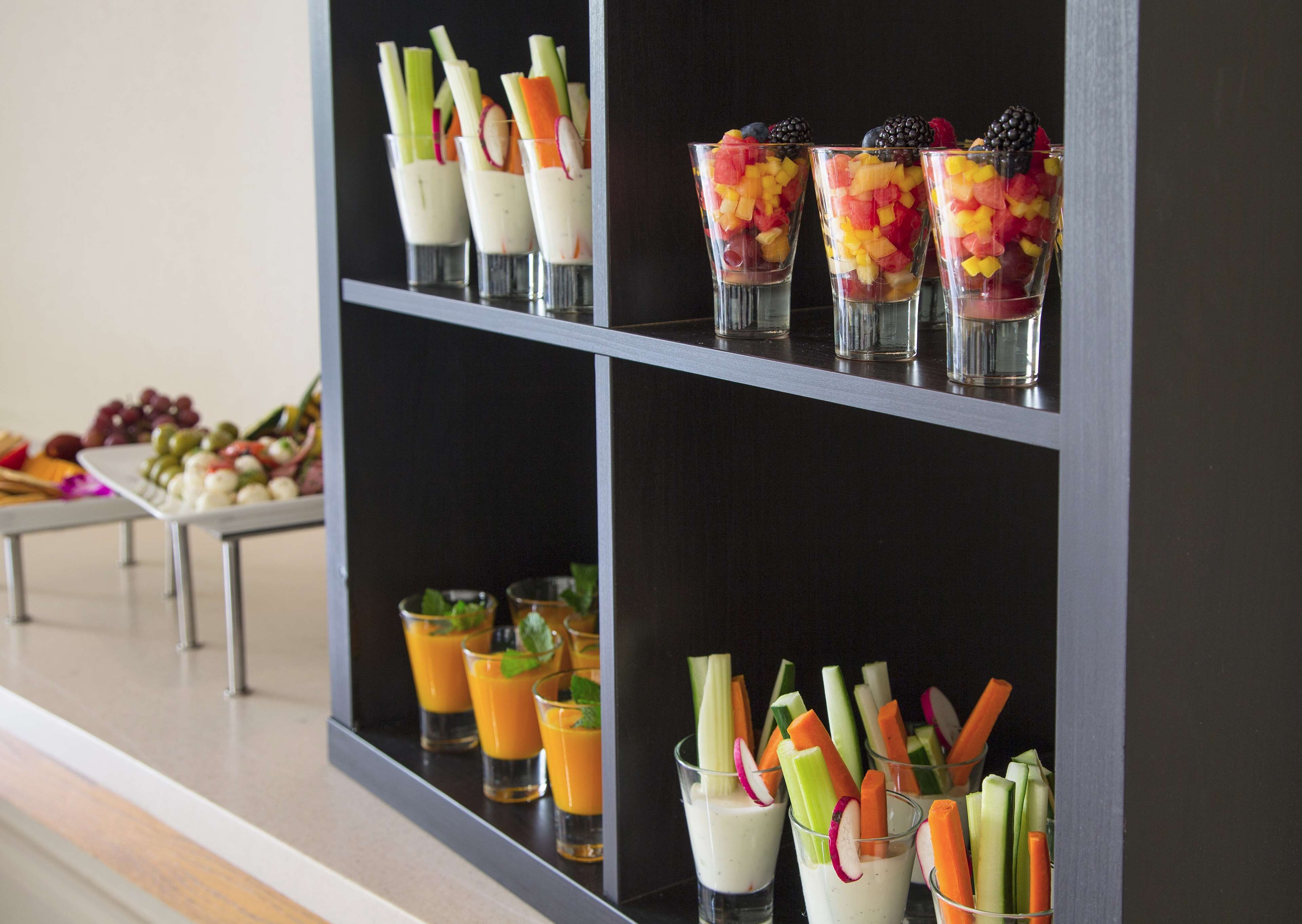 Buffet com diversas opções de comida, incluindo taças de fruta, palitos de legumes e um prato de queijos.