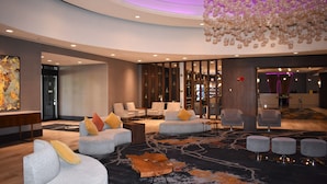 A modern lobby with seating areas, a large chandelier, and a reception desk.