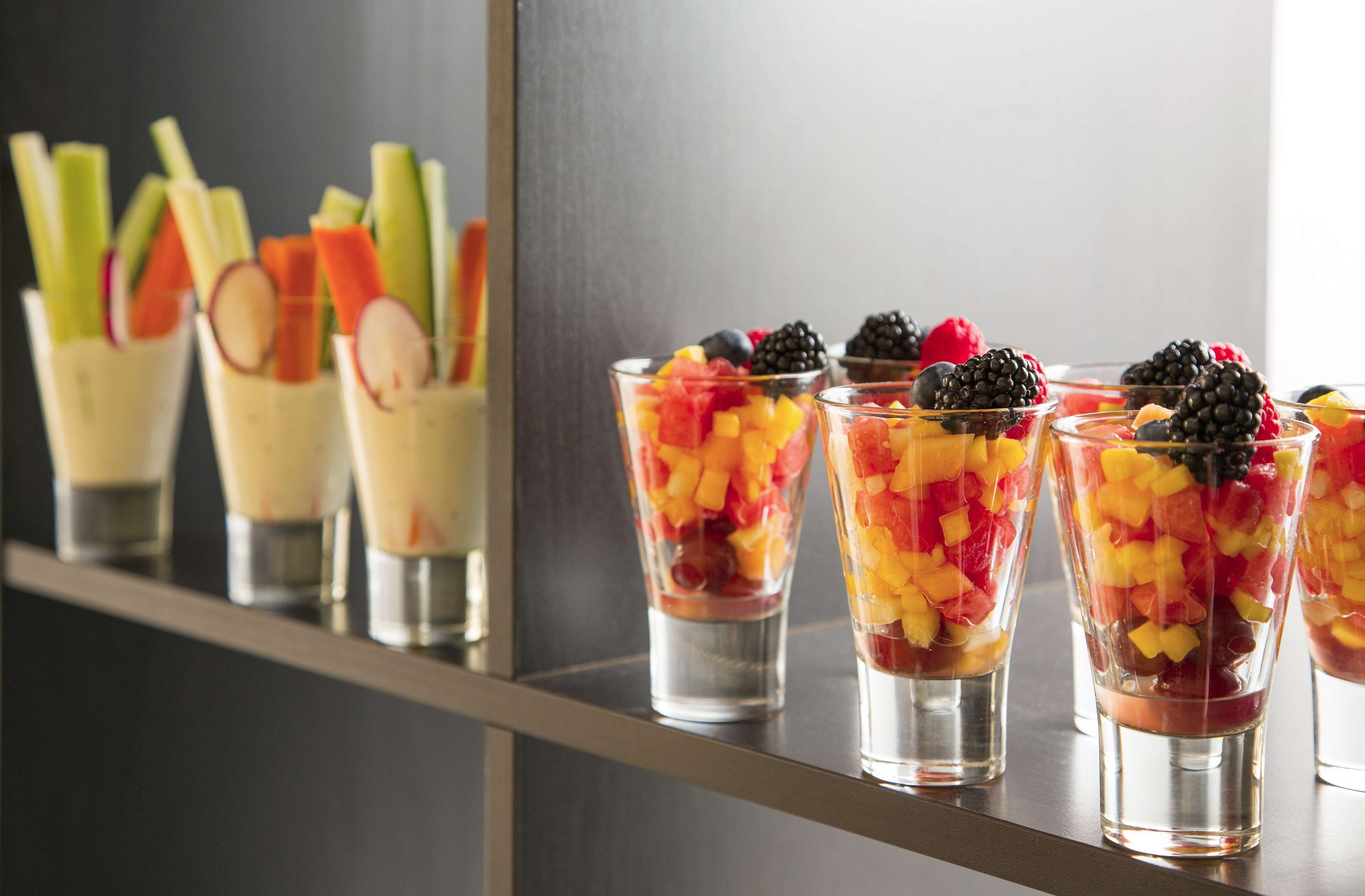 A row of clear glasses filled with fruit and berries, placed on a reflective surface.