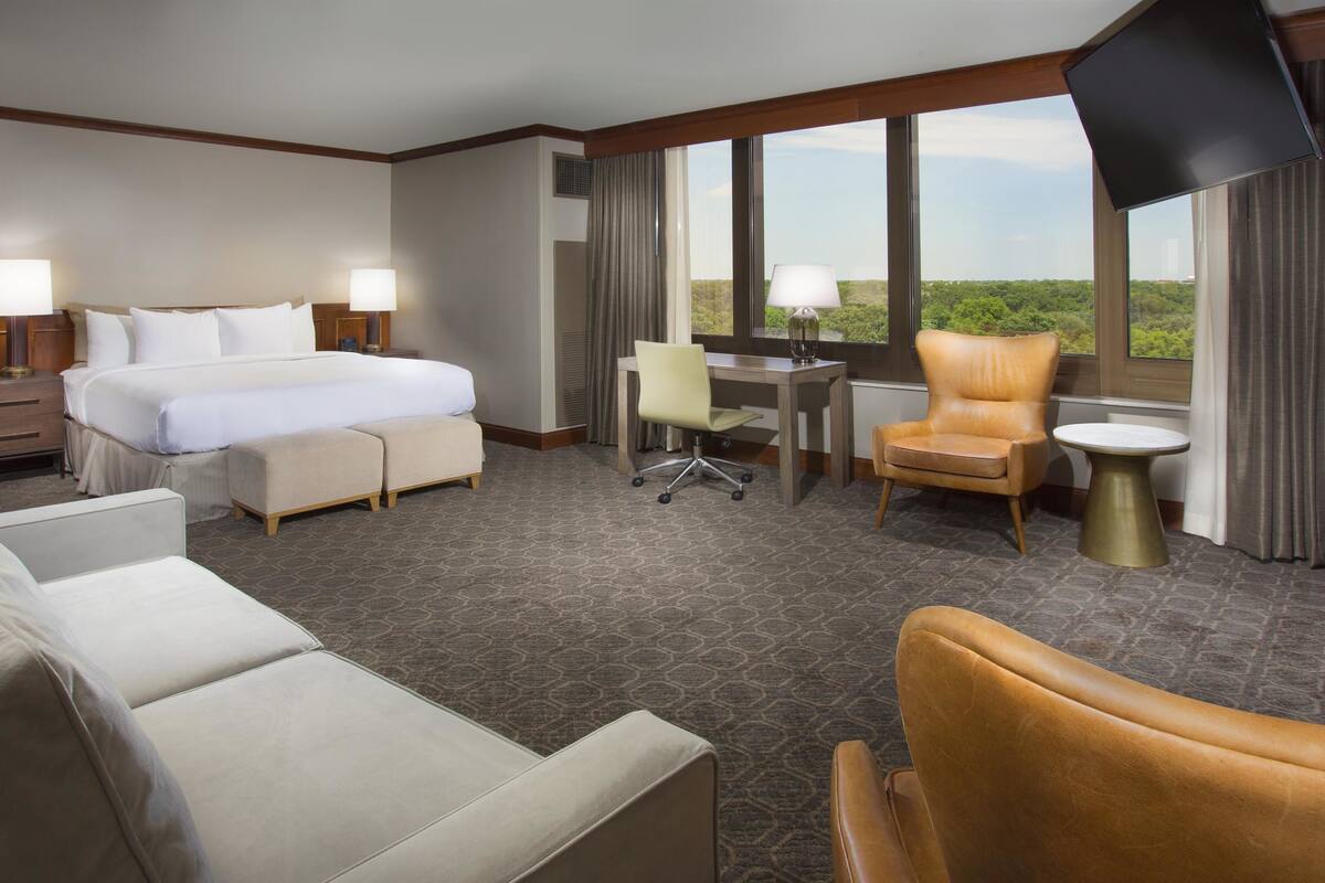 A hotel room with a bed, a desk, a chair, a sofa, and a TV.