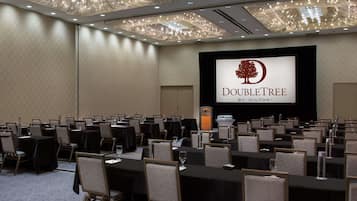 A conference room with rows of tables and chairs, a podium, and a screen displaying the DoubleTree by Hilton logo.