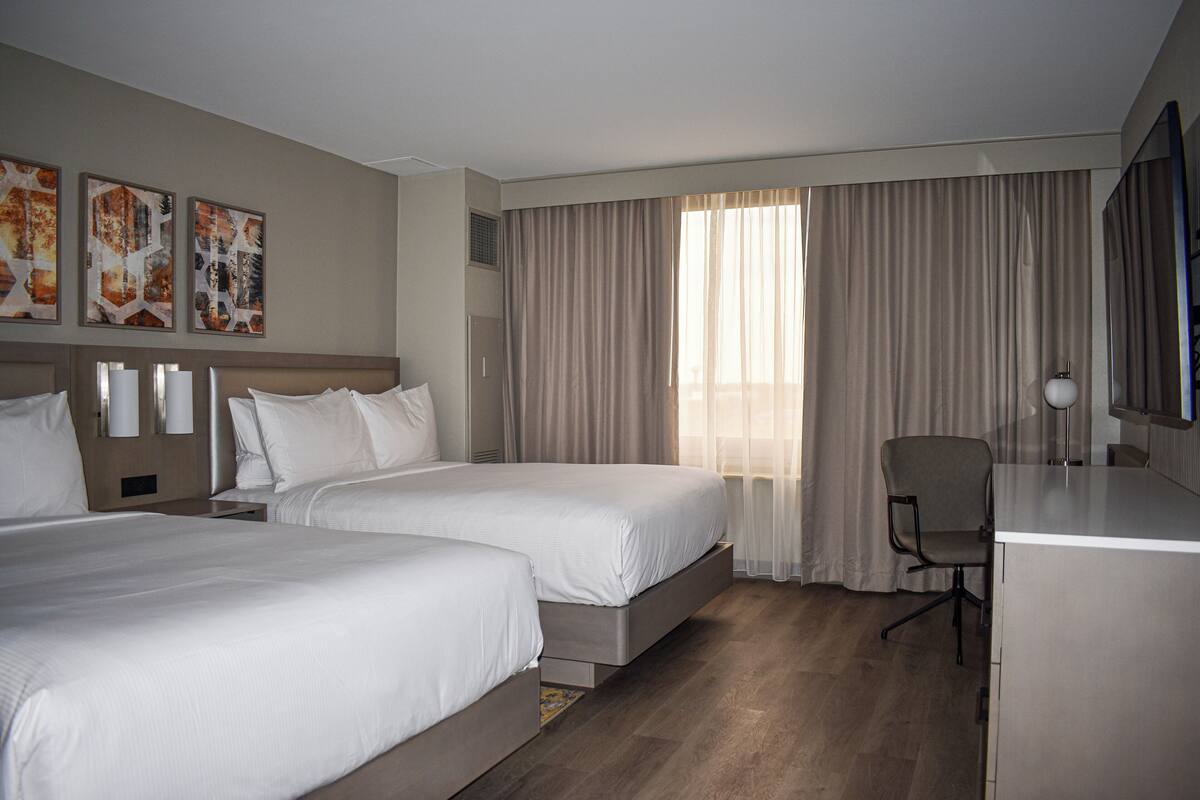 A hotel room with two beds, a desk, a chair, and a large window with curtains.