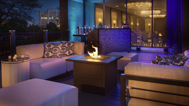 An outdoor seating area with a fire feature, white cushioned sofas, and a bar area with bottles.