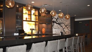 A bar area with a long counter, multiple hanging light fixtures, and a wall-mounted shelf with various items.
